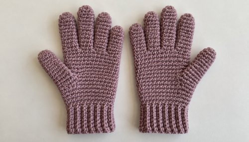 Cozy handmade crochet gloves in dusty pink resting on a wooden table