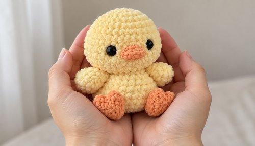 Hands holding a soft yellow crochet plushie chick
