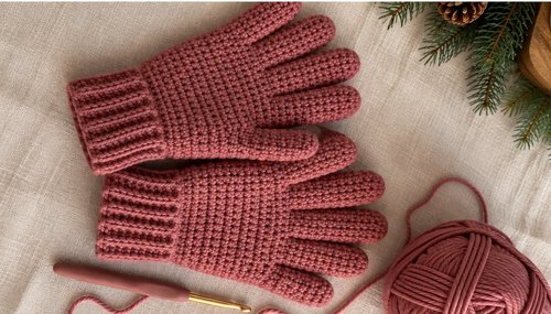 Crochet gloves flat lay with pink yarn and crochet hook