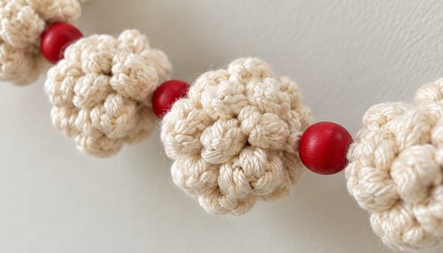 Close-up of crochet popcorn stitches with a red wooden bead cranberry on the strand